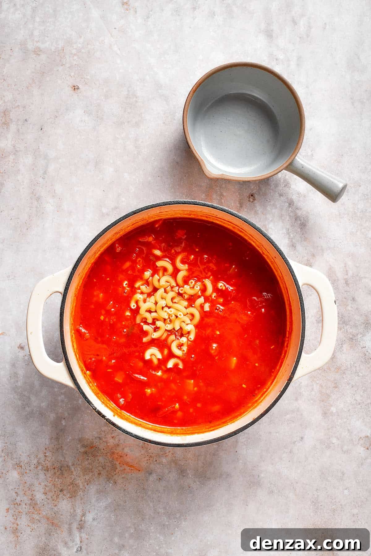 Elbow macaroni being added to a simmering pot of tomato Florentine soup.