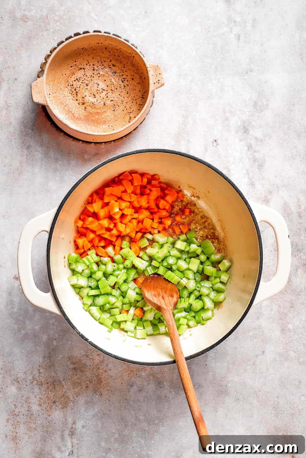 Chopped celery and carrots being added to the sautéed shallots and garlic in a soup pot.