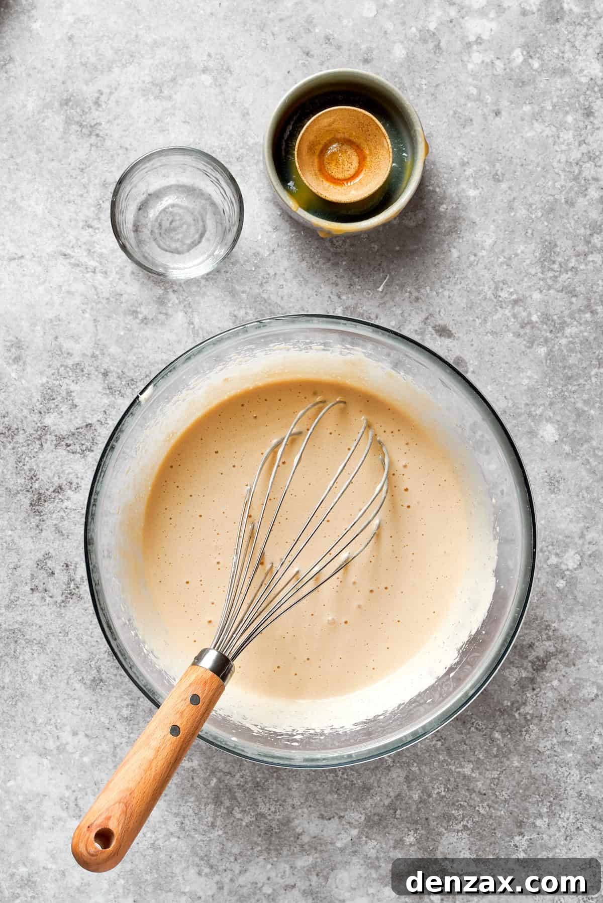 A whisk blending eggs, brown sugar, granulated sugar, applesauce, oil, and vanilla for the carrot cake wet ingredients.