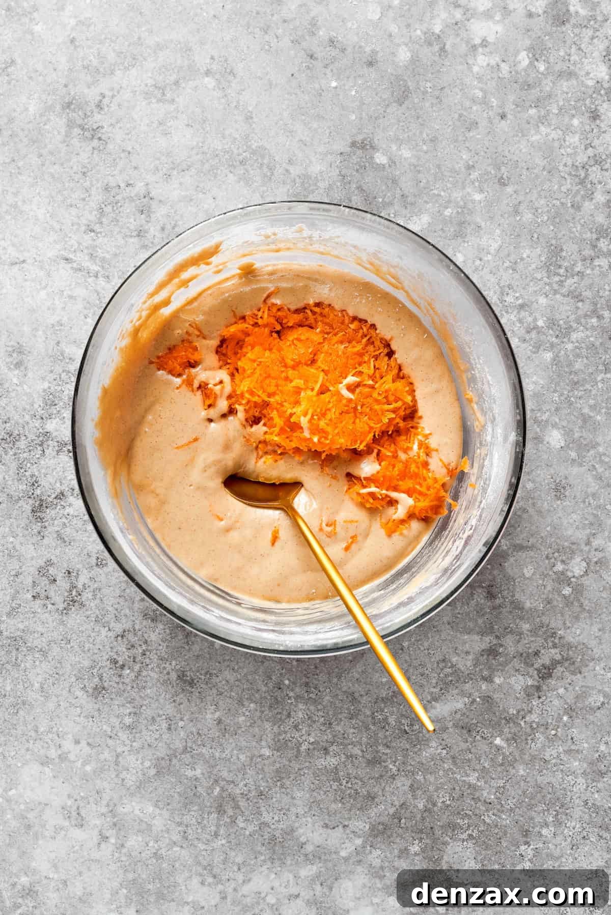 Finely grated carrots being folded into the prepared carrot cake batter.