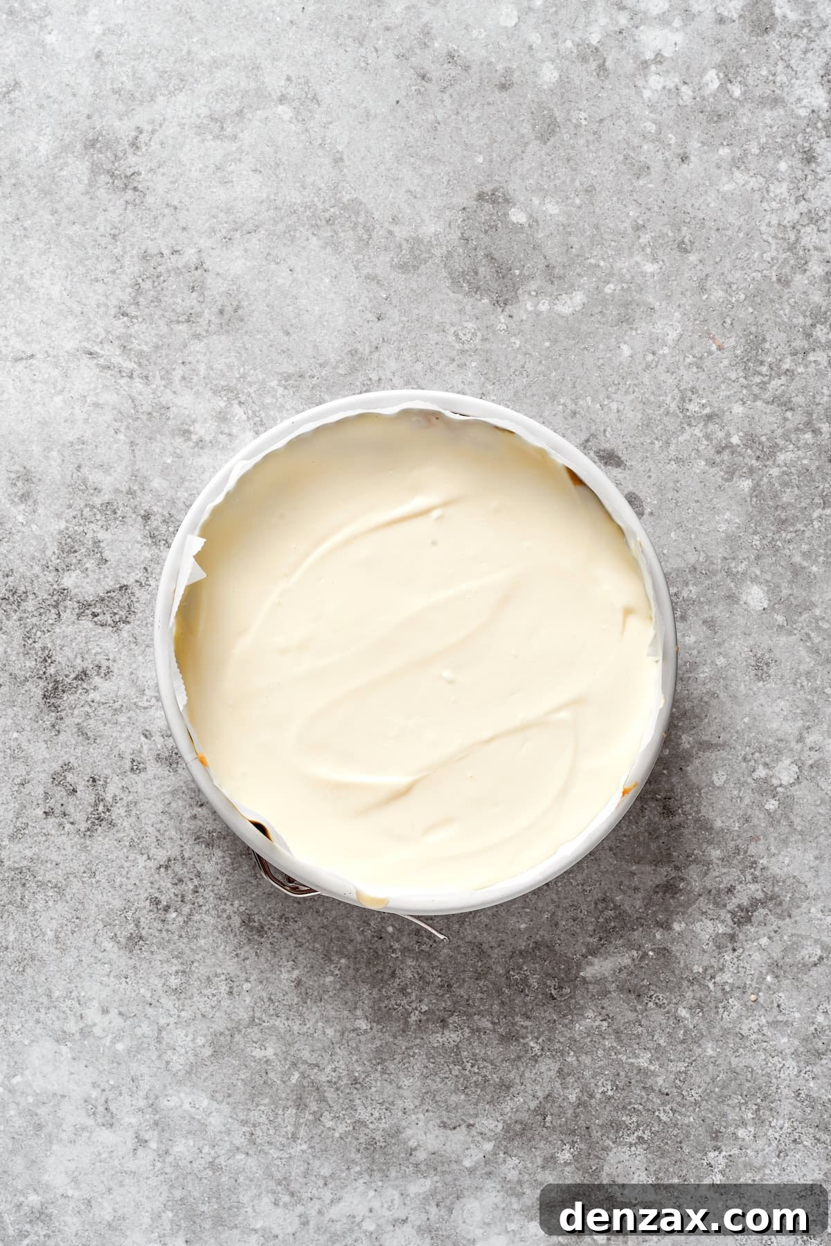Cheesecake batter being gently poured over the first layer of carrot cake batter in the pan.
