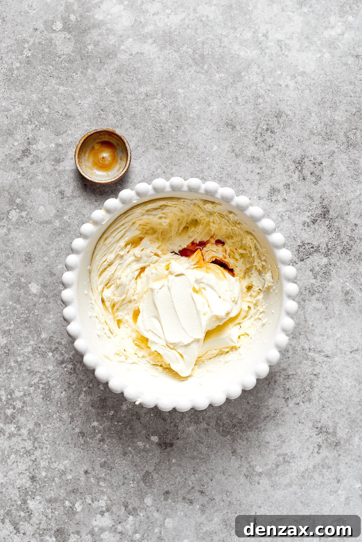 Vanilla extract being mixed into a bowl of fluffy cream cheese frosting.