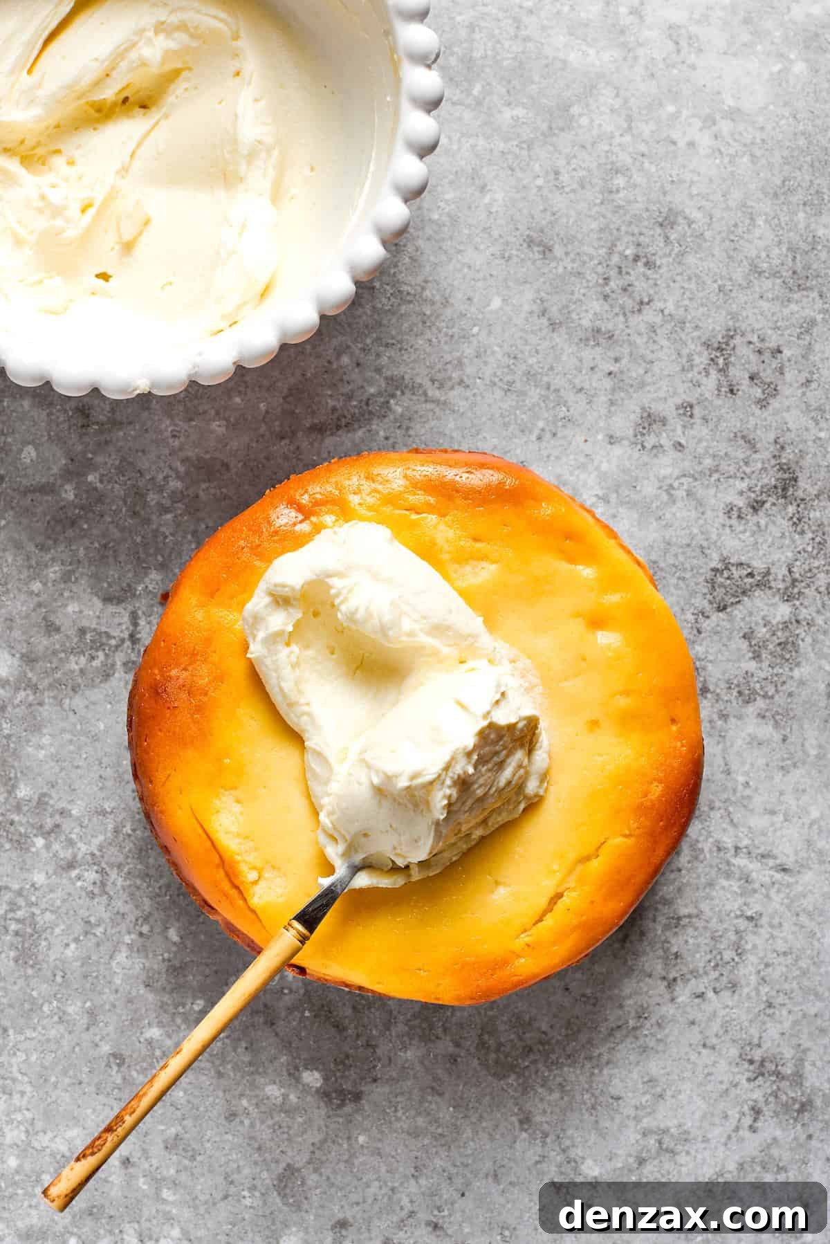 Cream cheese frosting being spread evenly over the top of a cooled carrot cake cheesecake.