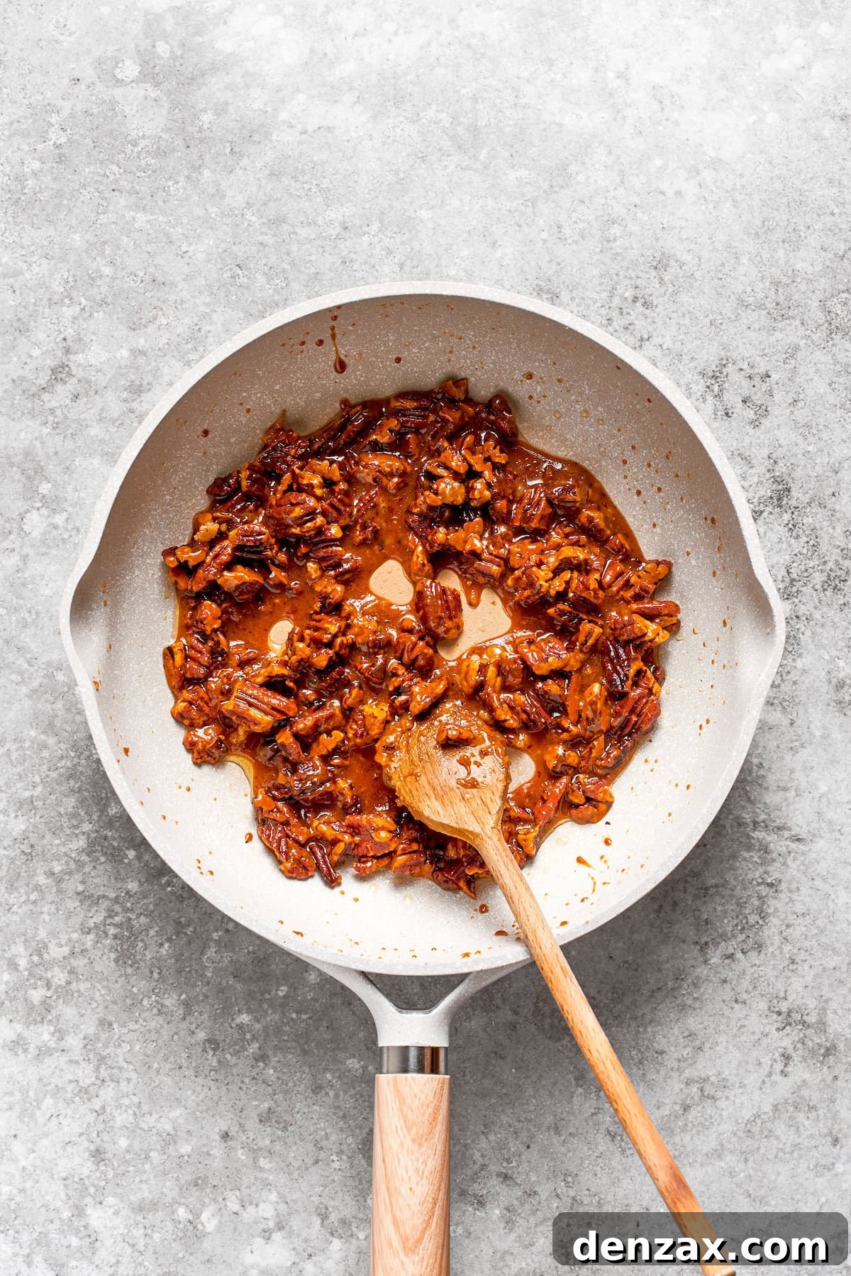 Chopped pecans being toasted with butter and sugar in a skillet to make caramelized pecans.