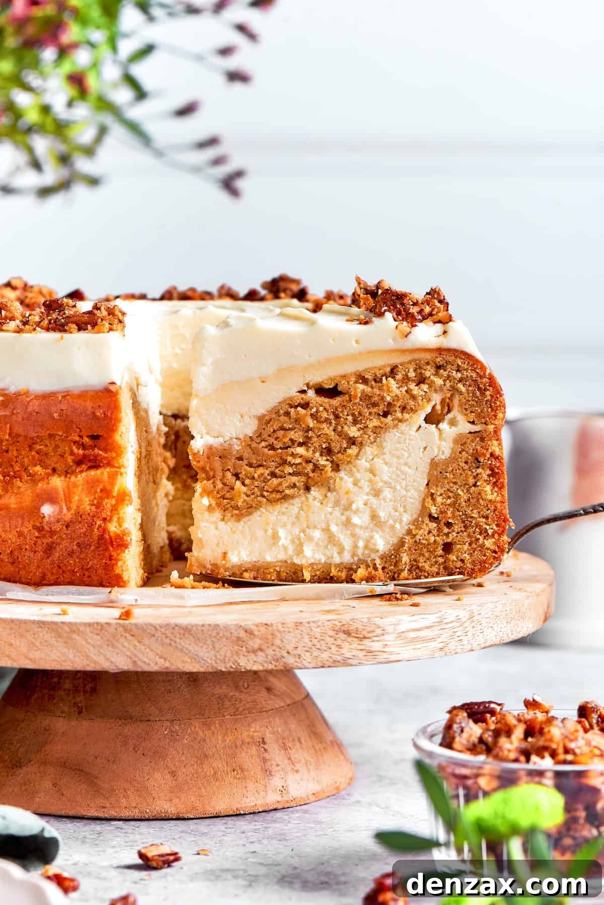 A perfectly baked and frosted carrot cake cheesecake with a slice being removed, showing its creamy layers.