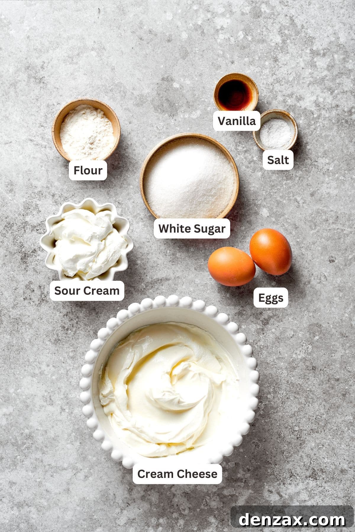 Ingredients for the cheesecake batter, such as cream cheese, sugar, flour, eggs, sour cream, and vanilla, are shown ready for use.