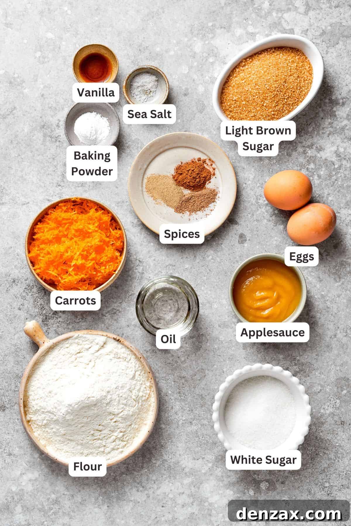 Carrot cake ingredients, including flour, baking powder, spices, eggs, sugars, applesauce, oil, vanilla, and grated carrots, are laid out.