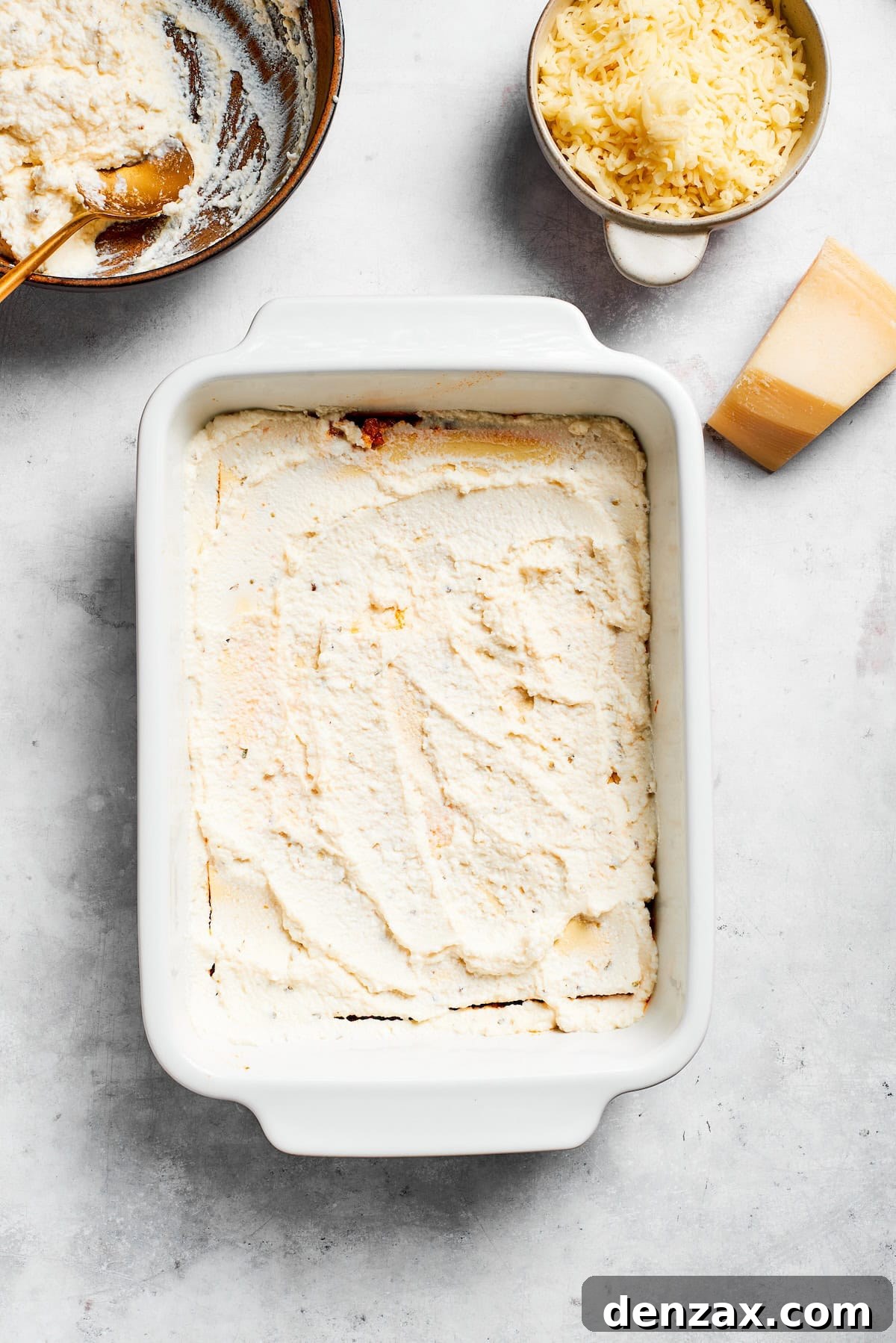 A smooth layer of ricotta cheese mixture spread evenly over lasagna noodles in a baking dish.