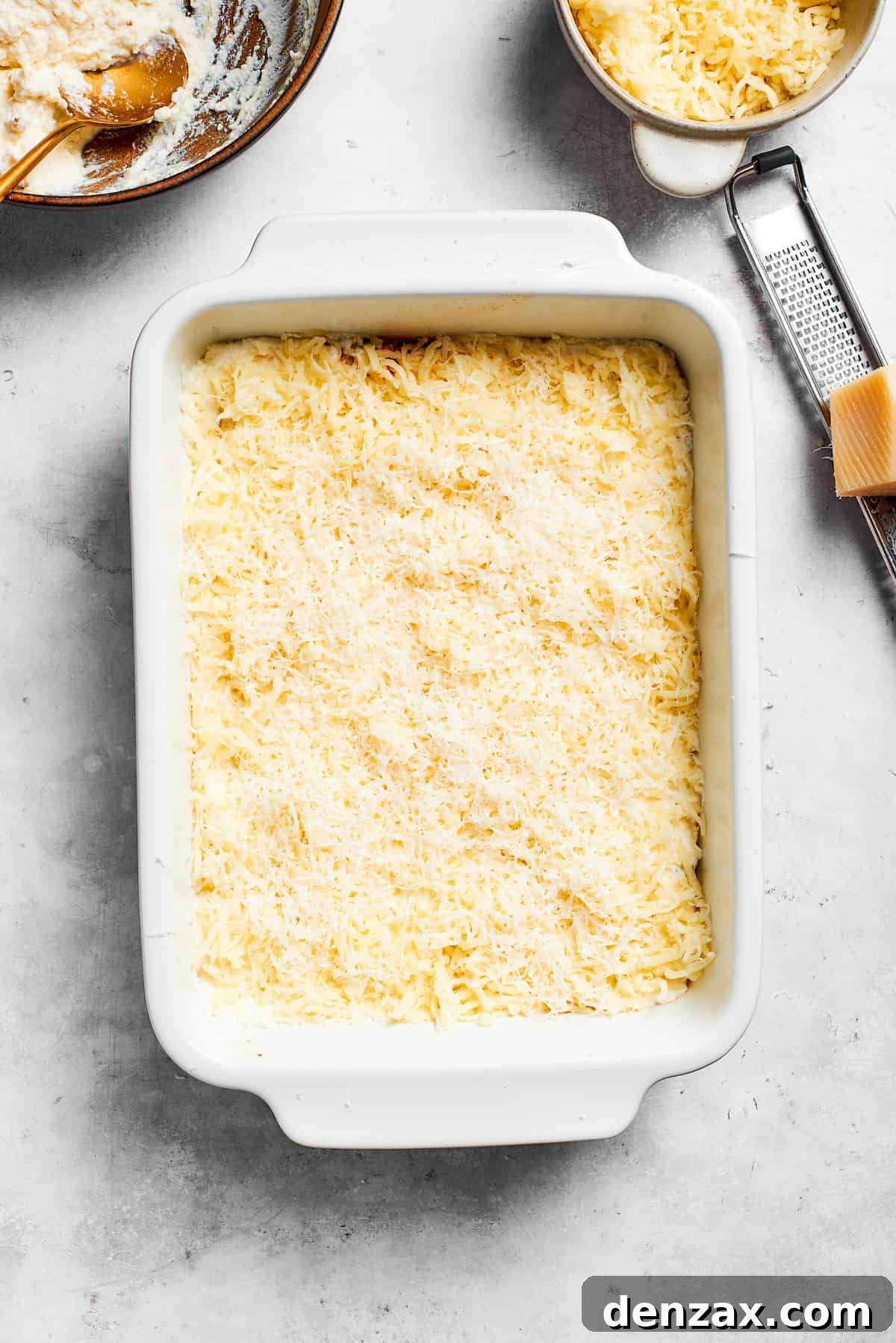 Shredded mozzarella and Parmesan cheese generously sprinkled over a layer of ricotta and noodles in the lasagna dish.