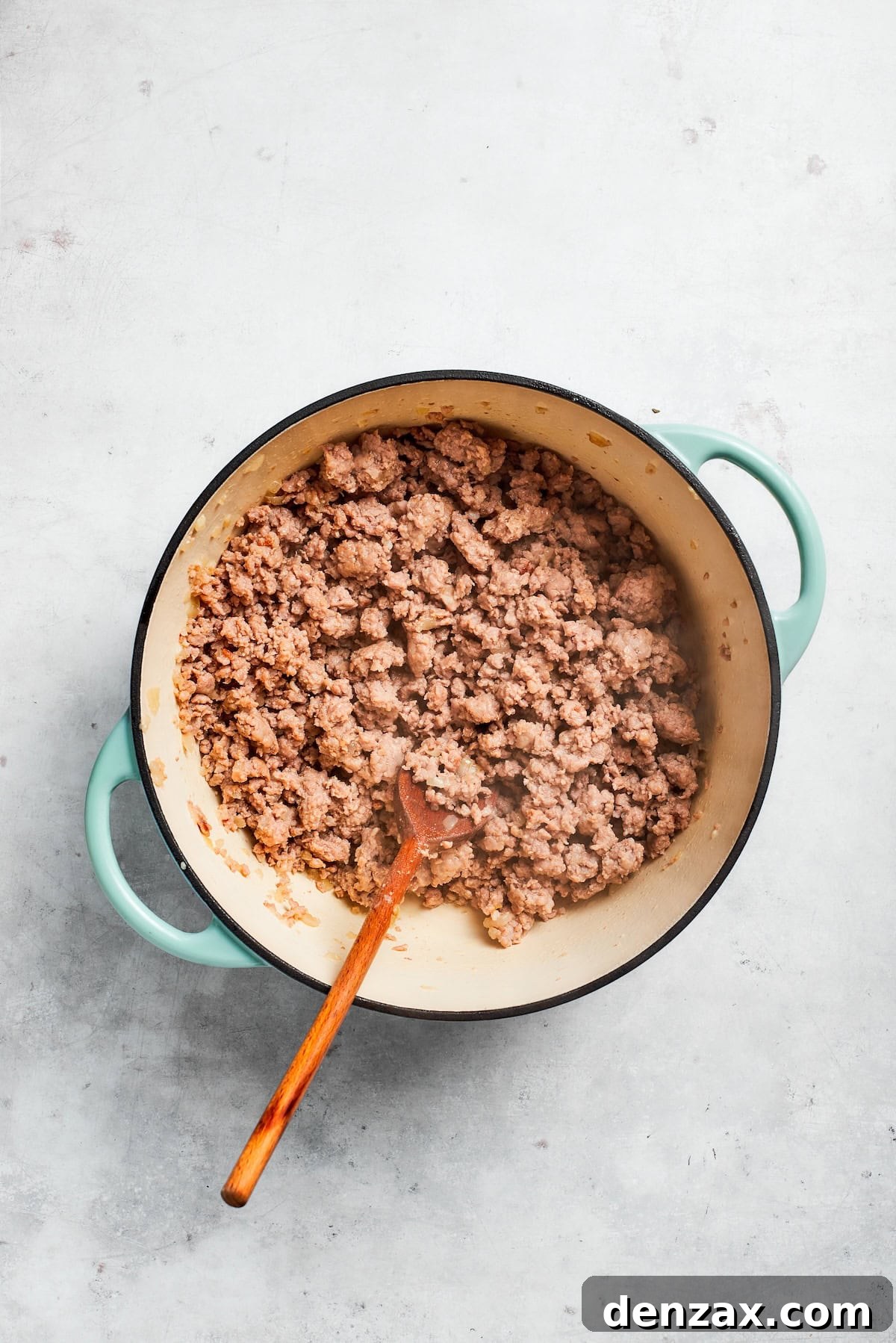 Ground beef cooking and browning in a skillet alongside sautéed onions and garlic.