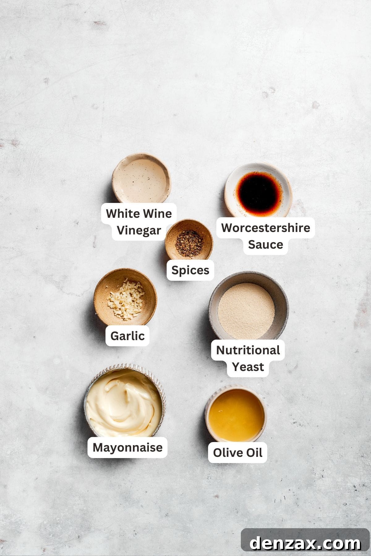 A selection of ingredients for the creamy Caesar dressing, including mayonnaise, lemon juice, Worcestershire sauce, and garlic cloves, are arranged and labeled.