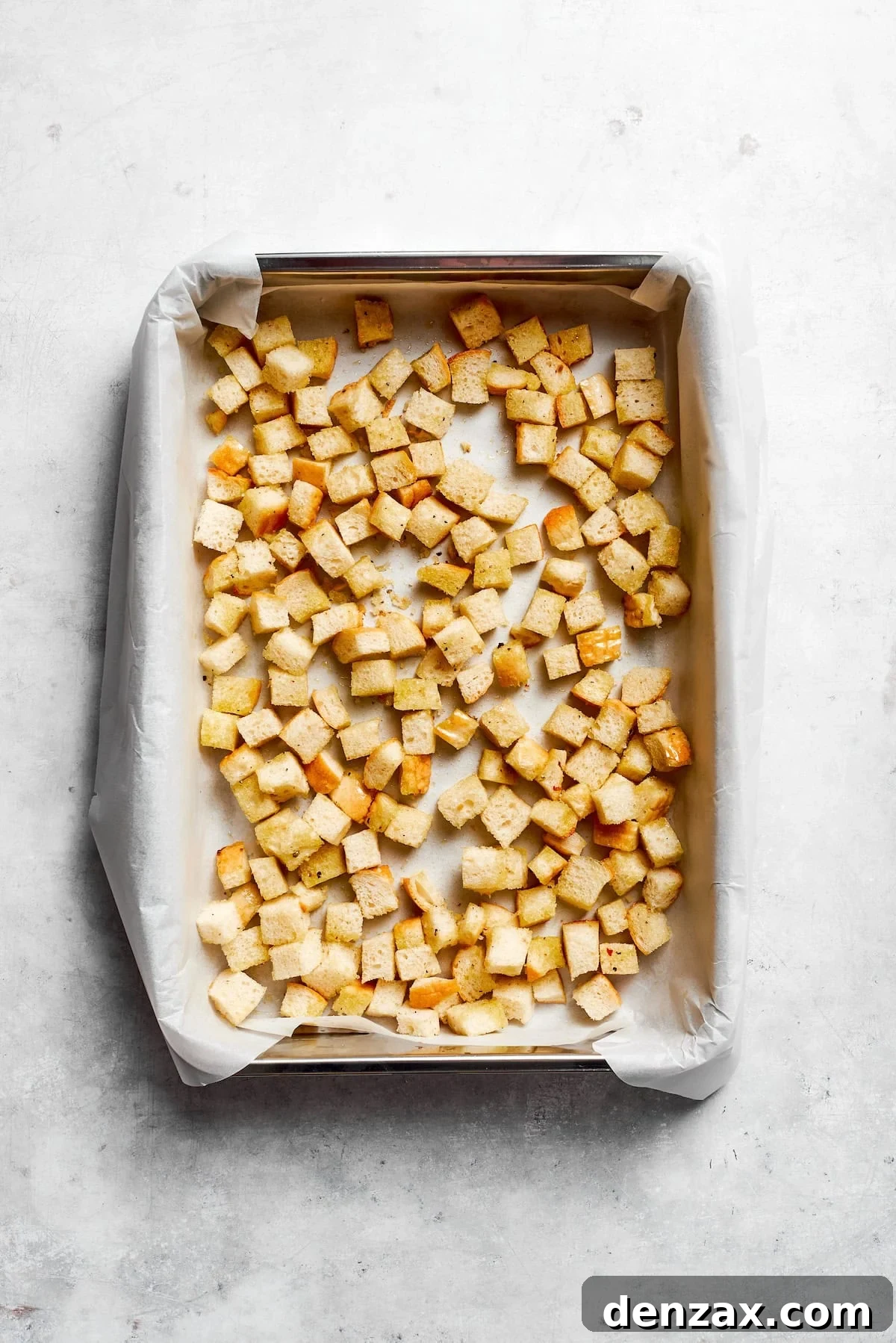 Freshly baked homemade croutons cooling on a parchment-lined baking sheet after being toasted to a golden crisp.