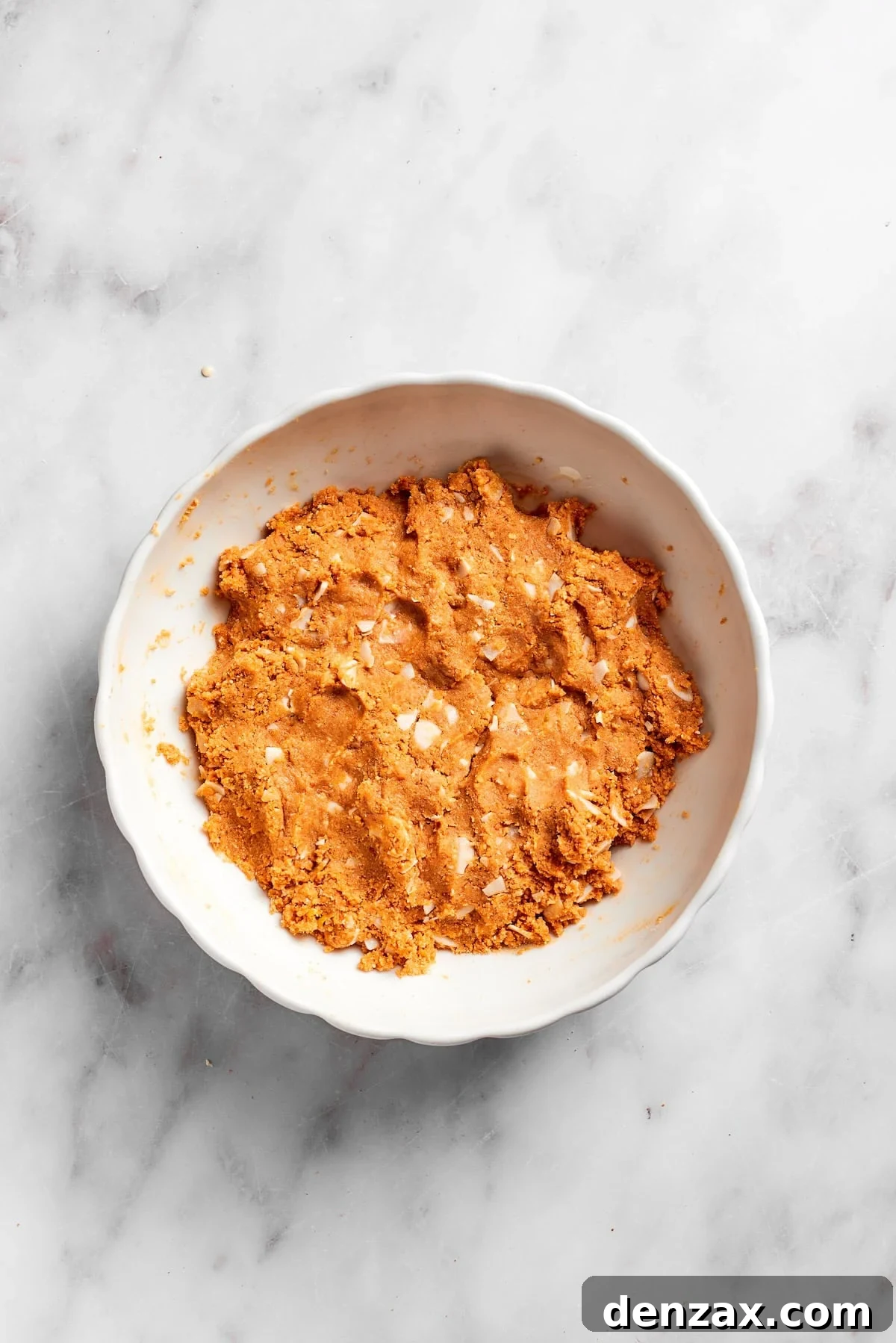 The graham cracker base mixture, now combined with wet ingredients, forms a cohesive, slightly sticky mass in a bowl, ready to be pressed into the pan.