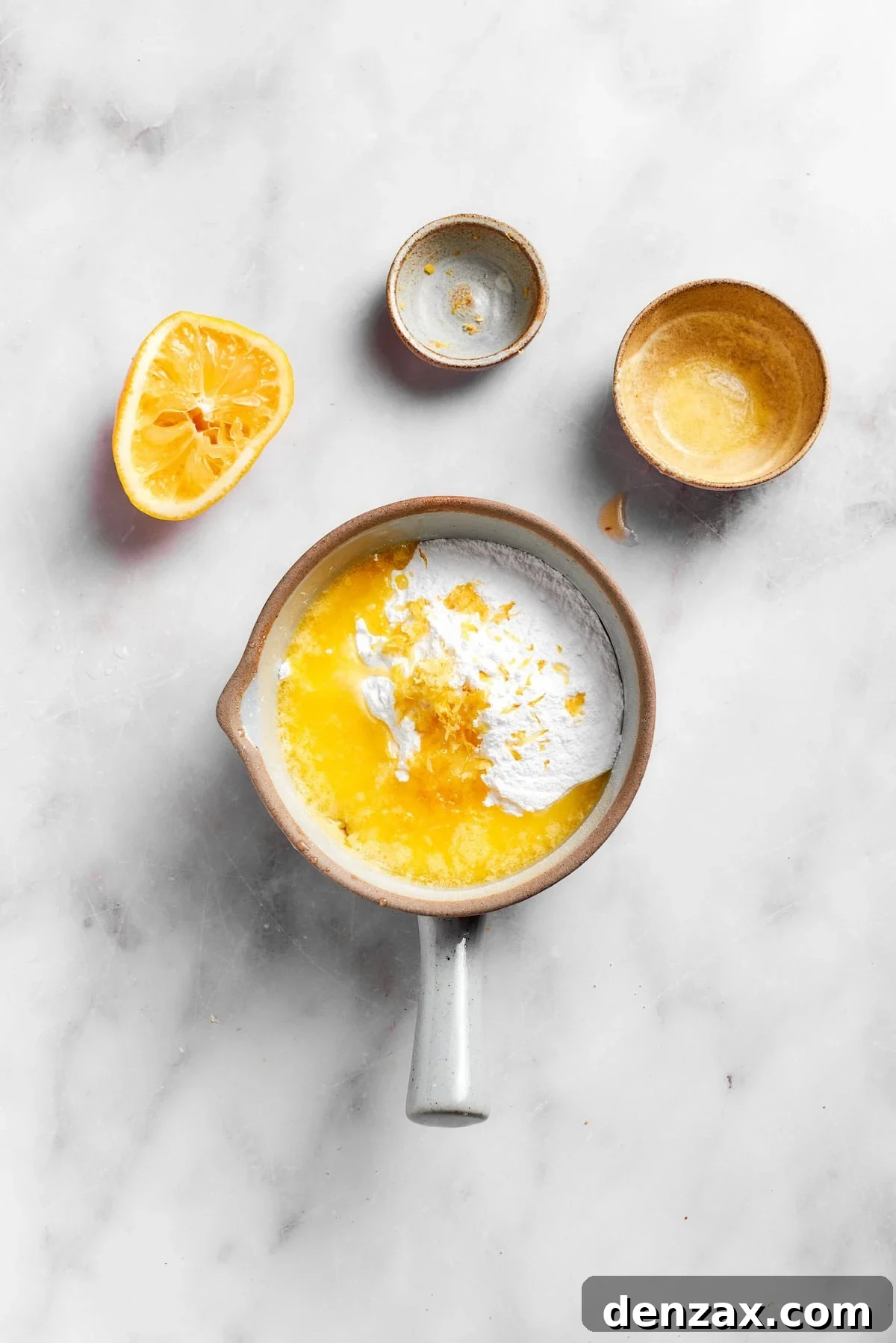 A whisk combines powdered sugar, lemon juice, melted butter, and lemon zest in a bowl, forming the vibrant lemon frosting.