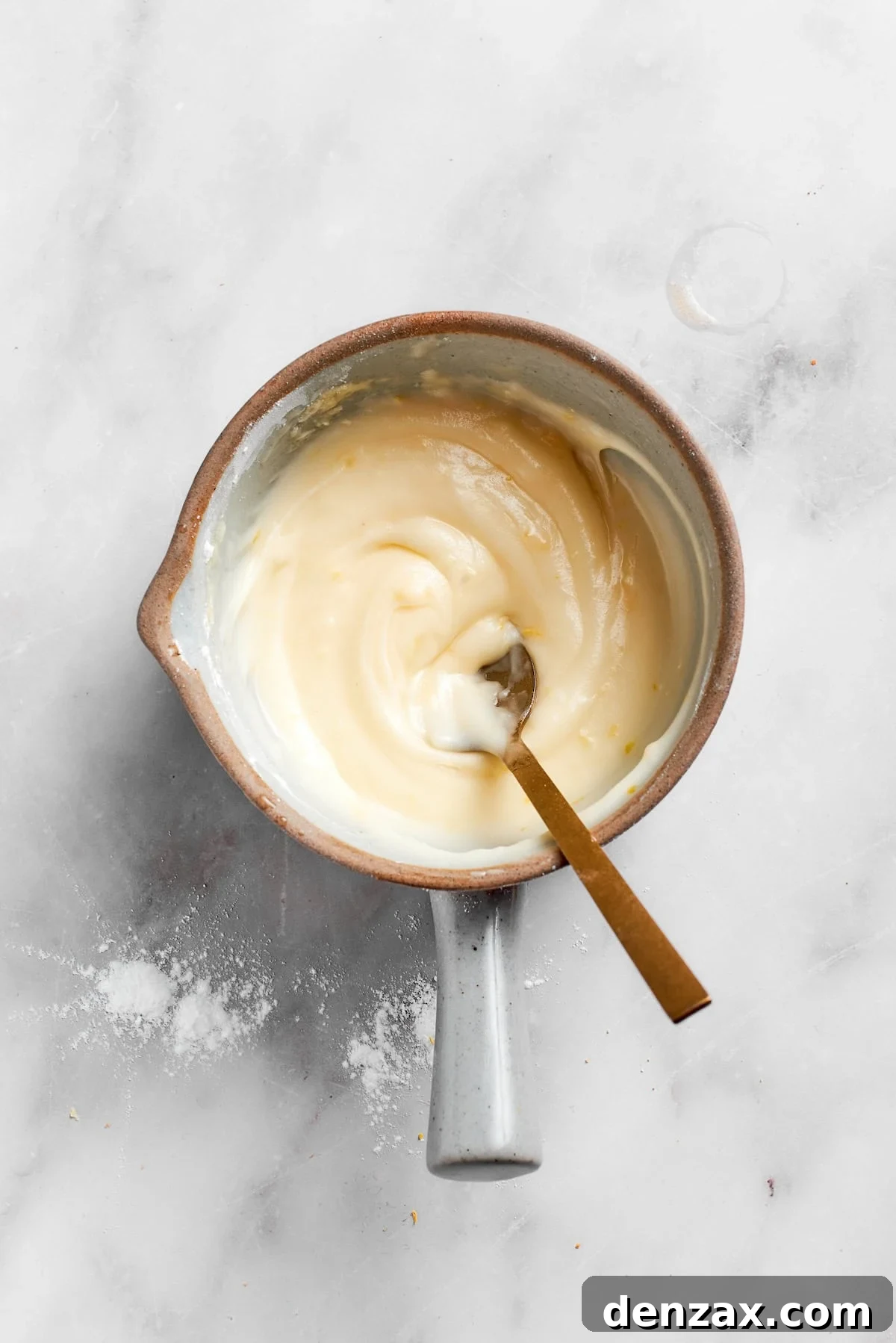 Close-up of a spoon stirring a bowl of creamy lemon frosting, showing its smooth, thick texture, indicating it's ready for spreading.