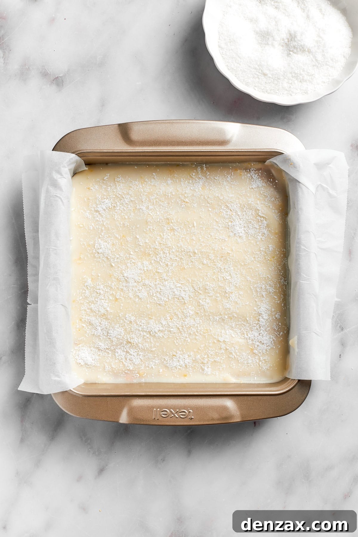 The completed lemon slice, with its smooth lemon frosting and a sprinkle of coconut, rests in the foil-lined pan, chilling in the refrigerator.