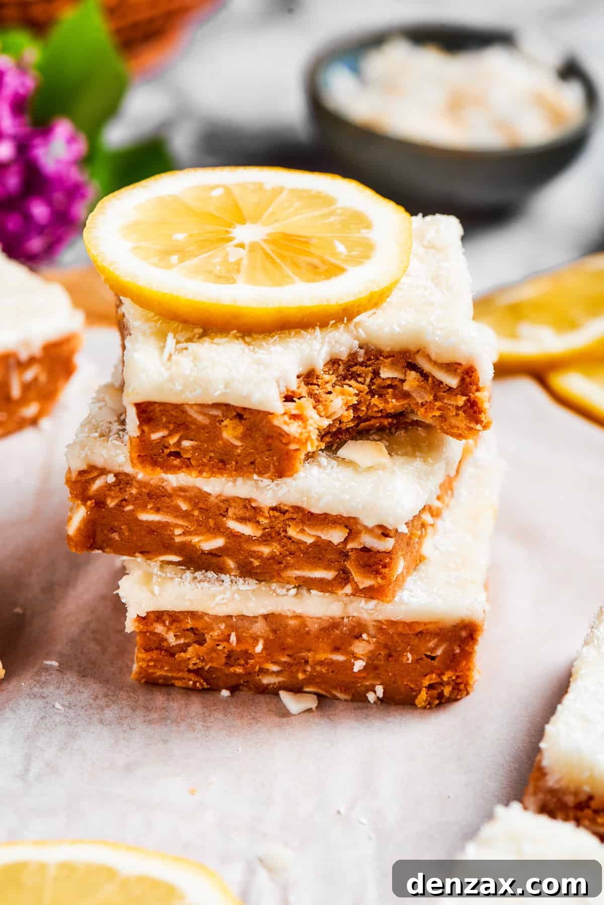 Three stacked lemon slice squares, with the top slice having a bite taken out, showing the layered texture of the crust and frosting. The vibrant yellow is inviting and hints at a delightful taste.