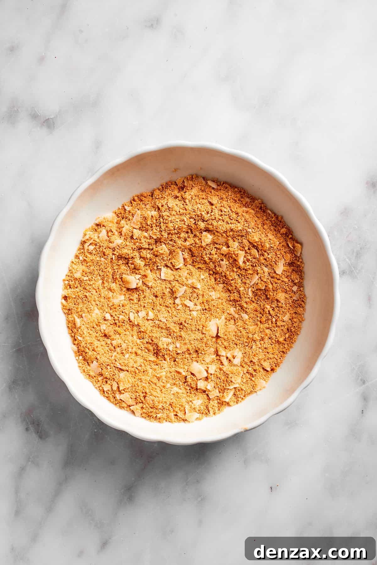 A bowl containing the mixed graham cracker and coconut crust base, showing a uniform texture, ready for the liquid ingredients.