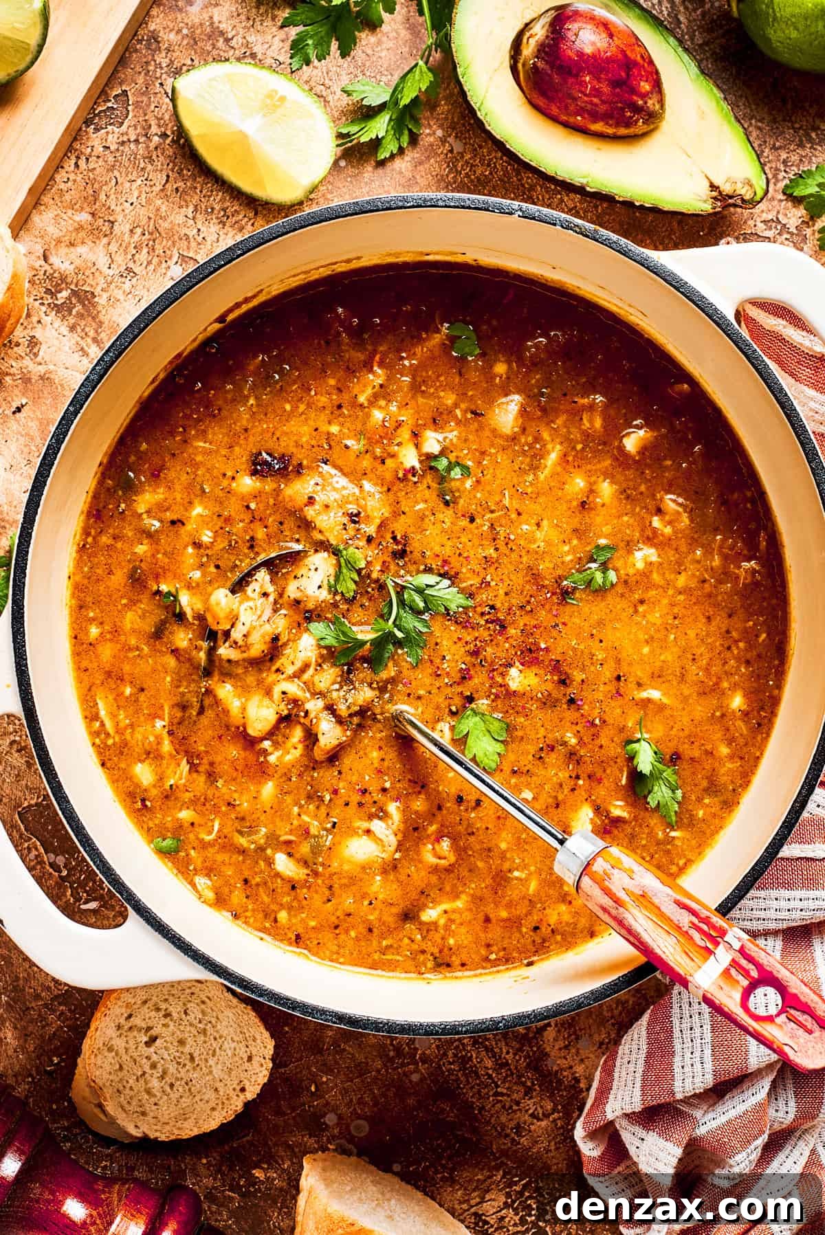 A large pot filled with spicy chicken and pinto bean soup, garnished with fresh cilantro and avocado slices. The soup is a rich, inviting green-red hue, indicating its savory depth and a hint of spice.