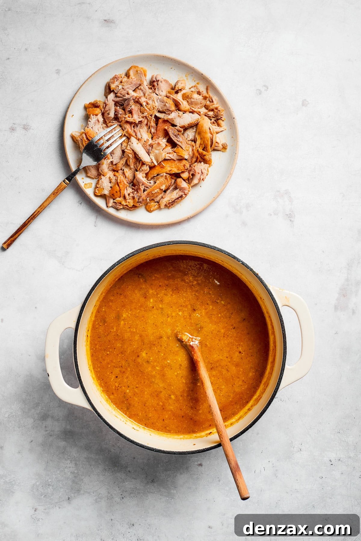 A plate of perfectly cooked and shredded chicken sits next to a large pot of simmering spicy chicken and pinto bean soup, ready to be incorporated back into the broth. The chicken is visibly tender and easy to pull apart.