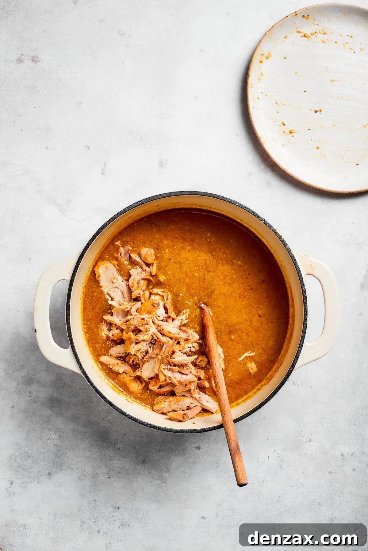 Shredded chicken pieces are being returned to the simmering pot of spicy chicken and pinto bean soup. The broth is rich and vibrant, with visible beans and chiles, preparing for the final melding of flavors.