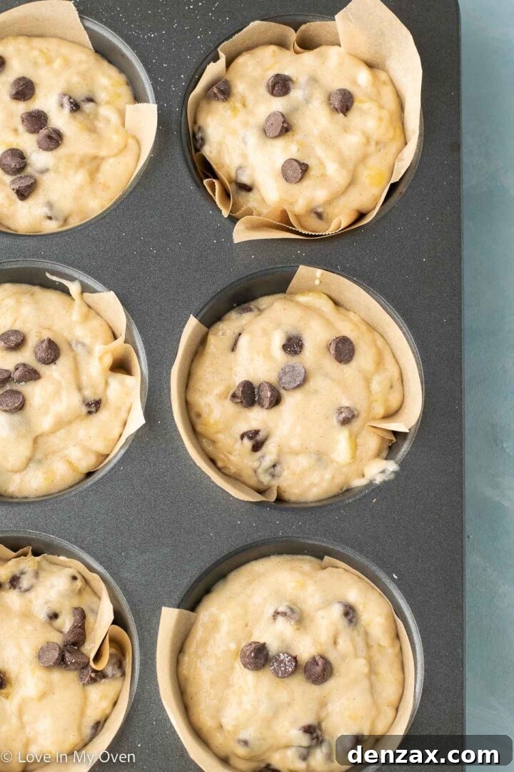 Jumbo banana chocolate chip muffin batter in tin, topped with extra chocolate chips and a sprinkle of sugar.
