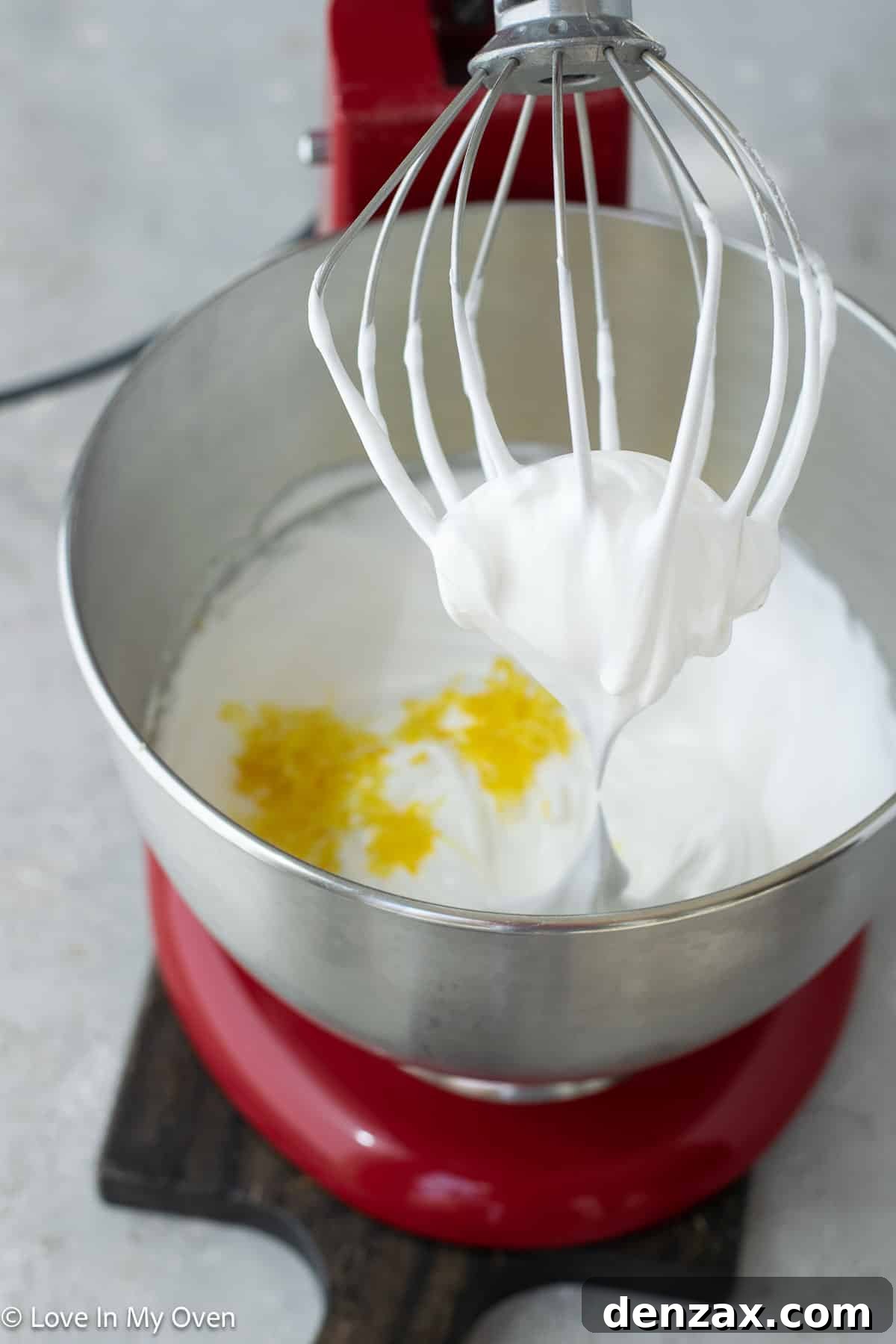 Meringue mixture being piped onto parchment paper, showing the creamy texture and potential for decorative swirls.