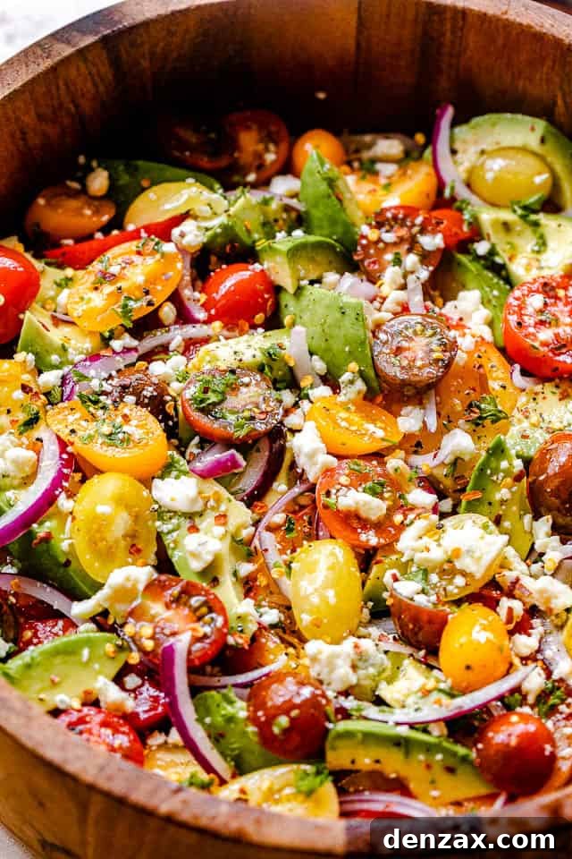 side shot of wooden salad bowl filled with tomatoes, onions, avocado, and bleu cheese