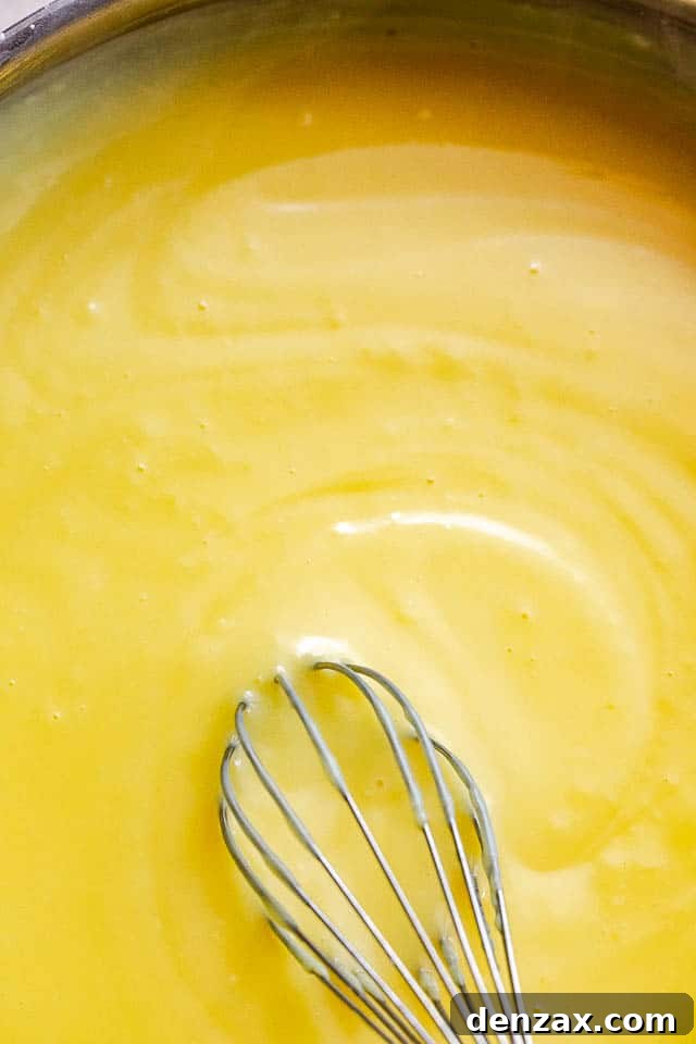 Close-up of a whisk stirring homemade vanilla pudding in a saucepan, showing its smooth texture.
