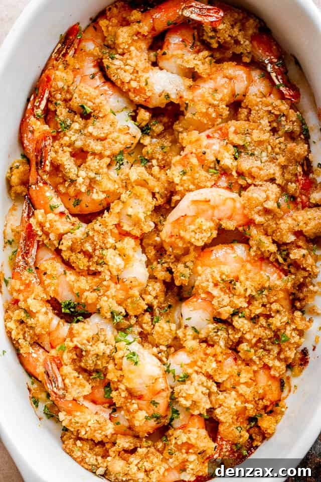 An overhead shot showcasing beautifully arranged shrimp in a pristine white oval baking dish, generously topped with a rich garlic butter and breadcrumbs mixture, ready to be served. The golden-brown crust hints at the deliciousness within.
