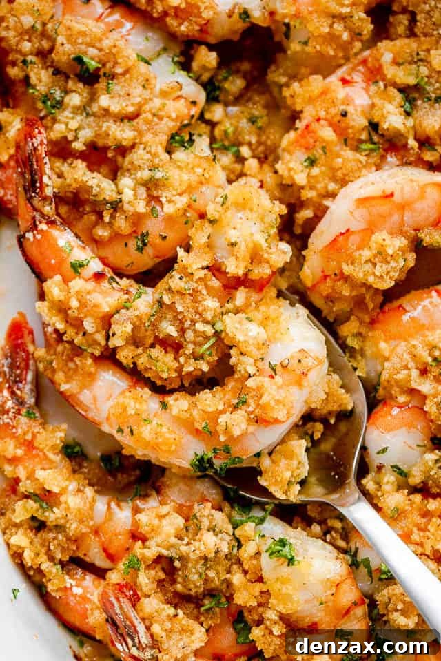 A silver spoon artfully scooping out a generous portion of Garlic Butter Baked Shrimp from the white oval dish, highlighting the tender shrimp and crispy topping, ready to be enjoyed.