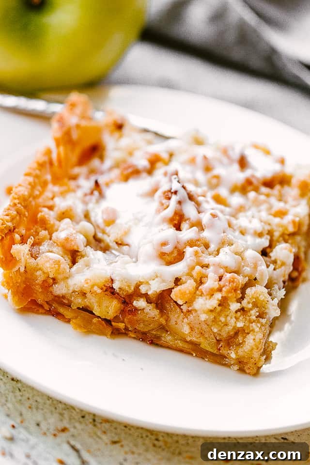 A perfectly portioned slice of Dutch apple slab pie on a white dessert plate, with a fresh green apple set alongside for garnish.