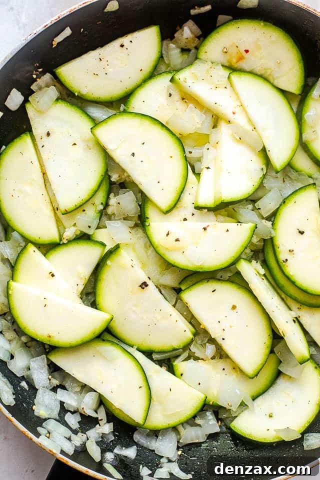 Frying thinly sliced zucchini and diced onion in a black non-stick skillet over medium heat.