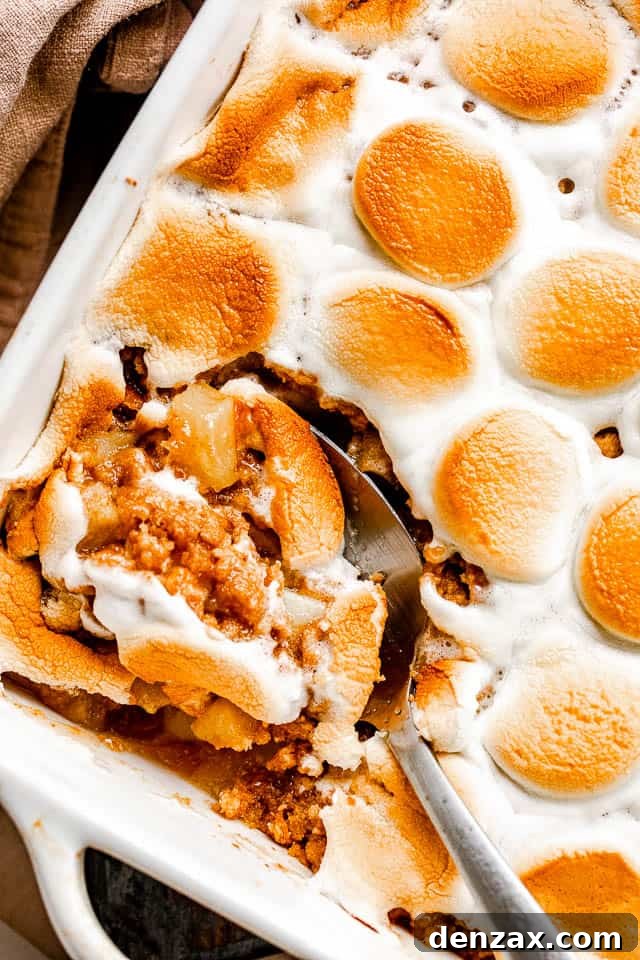 Overhead shot of a serving spoon scooping into a warm apple crumble with a graham cracker crust and melted marshmallows.