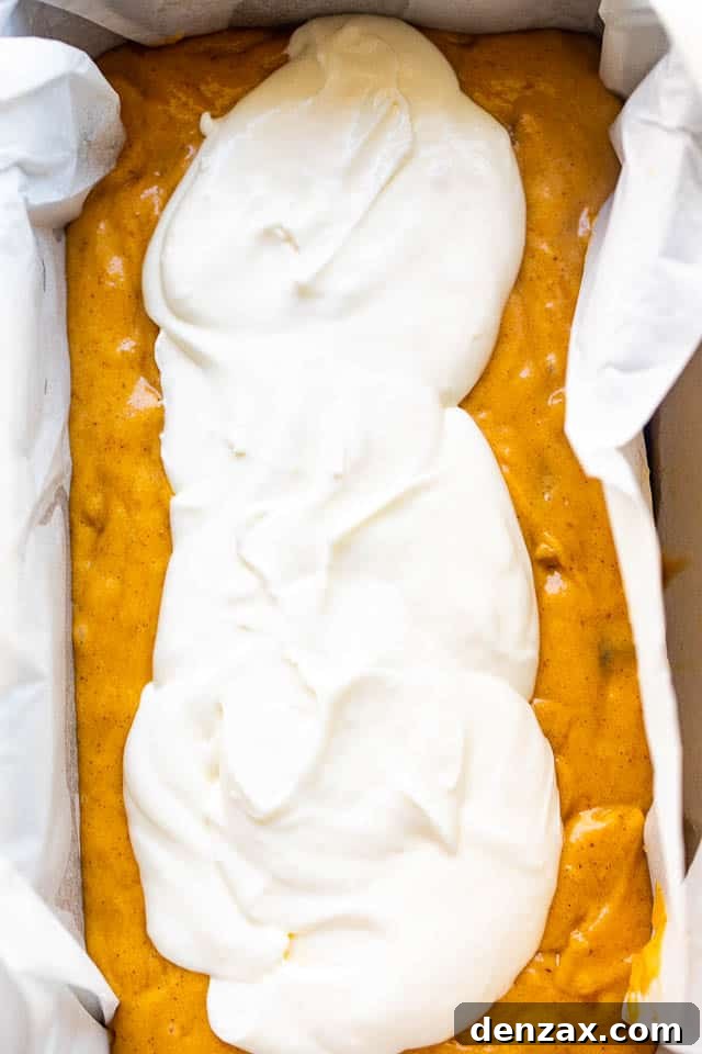 Loaf pan filled with pumpkin batter, ready for the cream cheese swirl to be added before baking, showing the start of a delicious bread.
