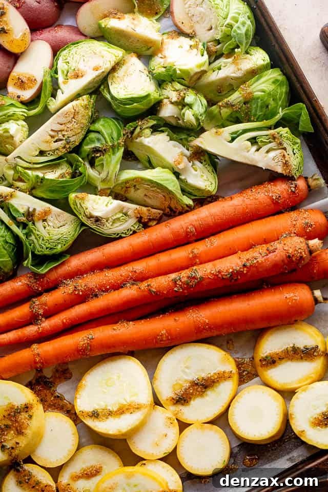 Raw carrots, Brussels sprouts, yellow squash, and fingerling potatoes, prepped and ready on a baking sheet before roasting