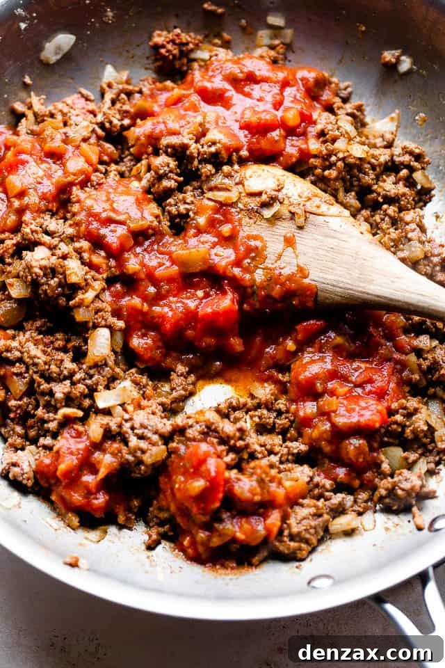 Overhead shot of ground beef, onions, and salsa simmering in a large skillet, cooking the flavorful burrito filling.
