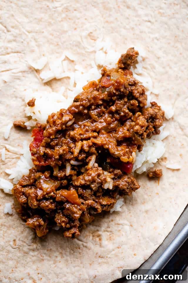 Flour tortilla topped with a layer of cooked rice and a generous portion of beef and bean filling, ready for folding.