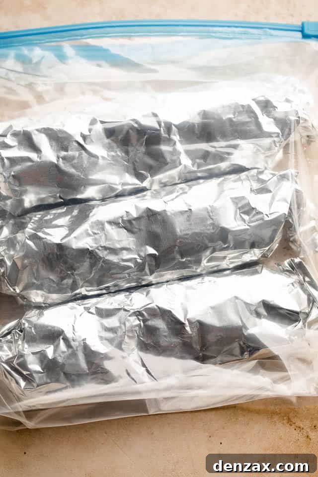Individual beef and bean burritos, neatly wrapped in foil and stacked inside freezer-safe ziploc bags for convenient storage.