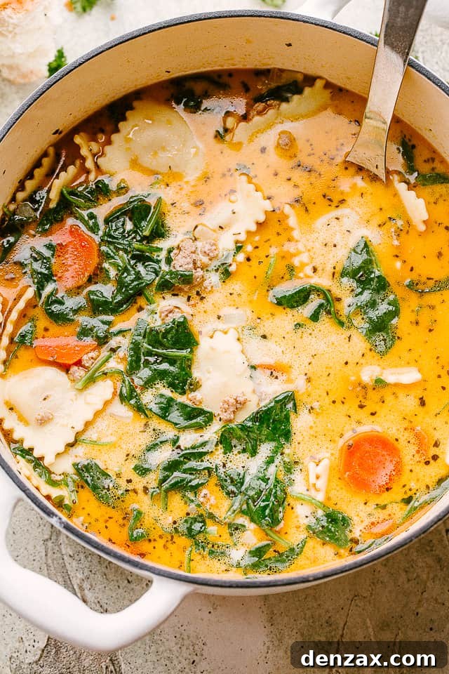 An overhead shot of a large pot filled with creamy ravioli soup, showing the rich texture and an abundance of ravioli and spinach.