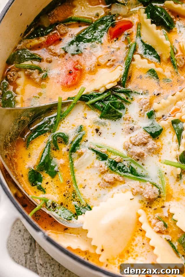 A close-up view of creamy ravioli soup with vibrant spinach leaves and plump ravioli, highlighting the rich texture and inviting steam.