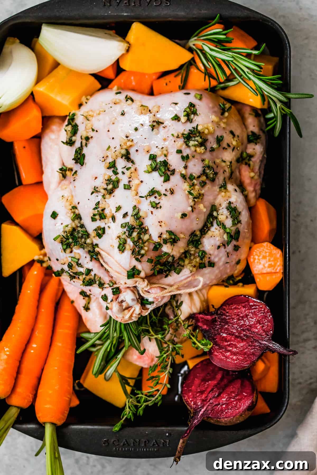 Whole raw broiler chicken in a baking pan with root vegetables.