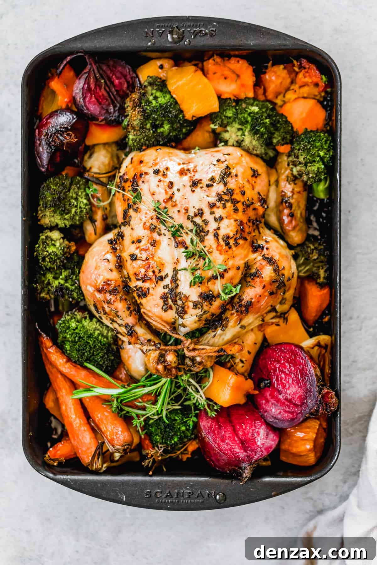 Whole roast chicken with fall vegetables on a sheet pan.