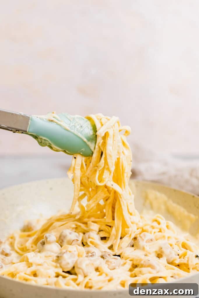 A Pair of Tongs Grabbing a Bunch of Fettuccine Noodles Covered in Alfredo