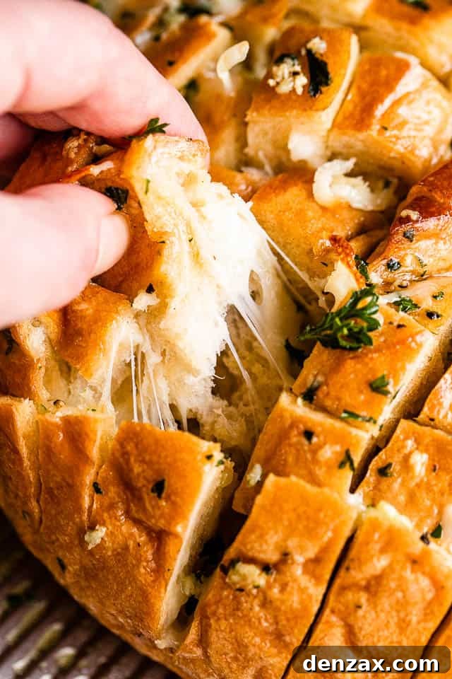 A hand pulling apart a section of golden-brown cheesy garlic bread, revealing melted cheese and fragrant herbs.