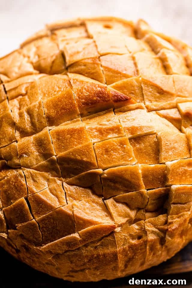 A round loaf of bread with a crosshatch pattern scored into its top surface, ready for stuffing.