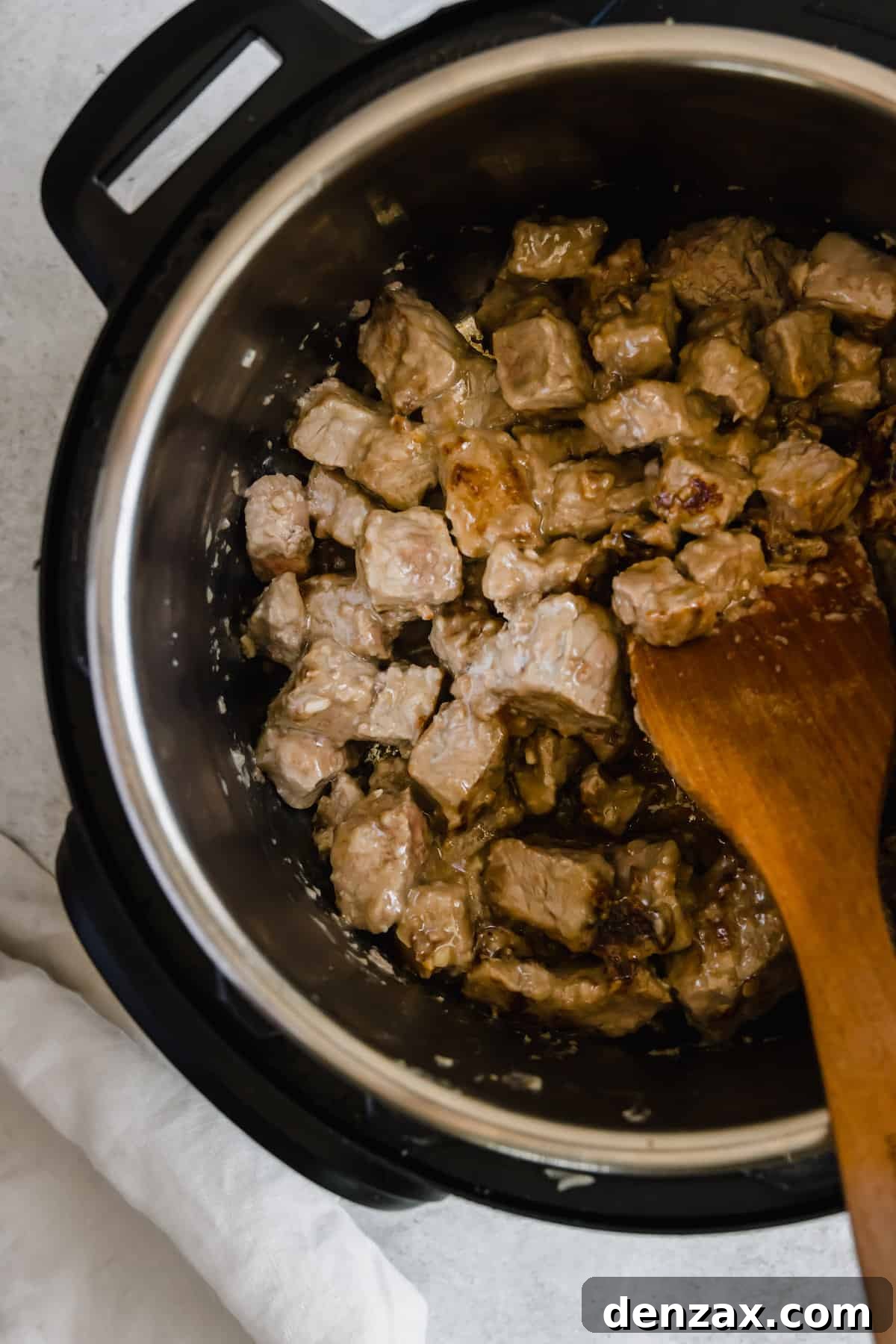 Beef Being Stirred Around in the Instant Pot by a Wooden Spoon