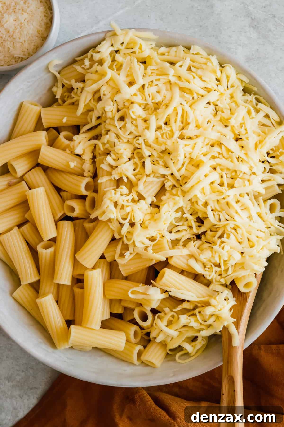 Cooked rigatoni noodles mixed with shredded mozzarella cheese in a large mixing bowl, ready for the next step of the casserole assembly.