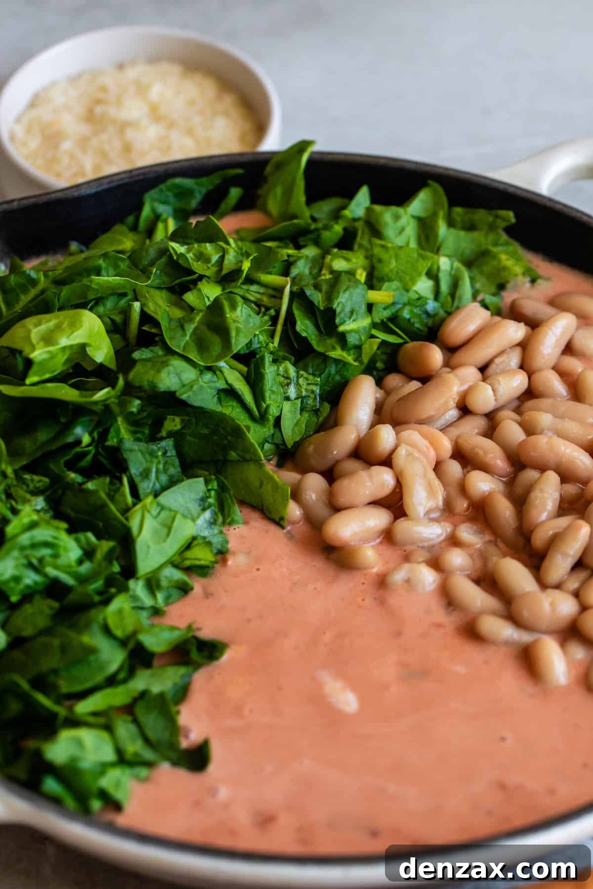 A skillet filled with a creamy Tuscan tomato sauce, enriched with fresh spinach and cannellini beans, simmering on the stovetop.