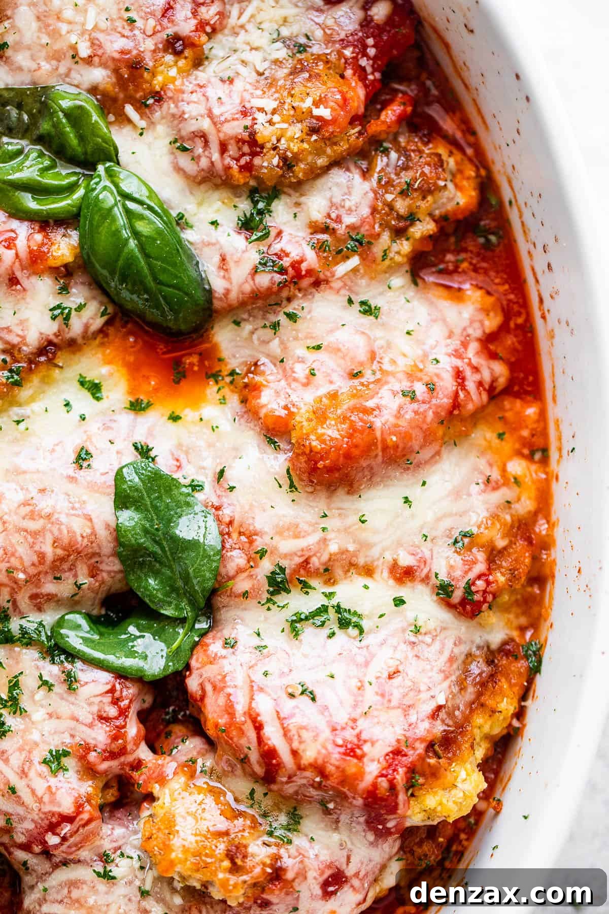 Close-up overhead shot of baked pork parmigiana topped with melted mozzarella cheese and fresh basil leaves, ready to serve.